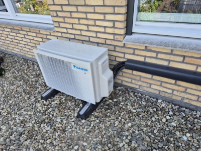 Daikin airco buitenunit op grind dak tussen twee ramen met anthraciet koelgoot 