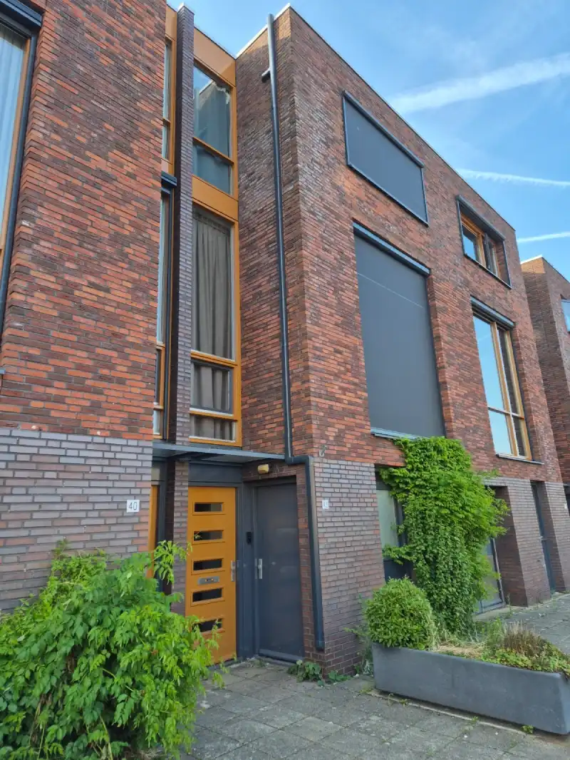 Antraciete koelgoot van dak tot grond met twee aansluitingen voor binnenunits tegen voorgevel van bakstenen huis