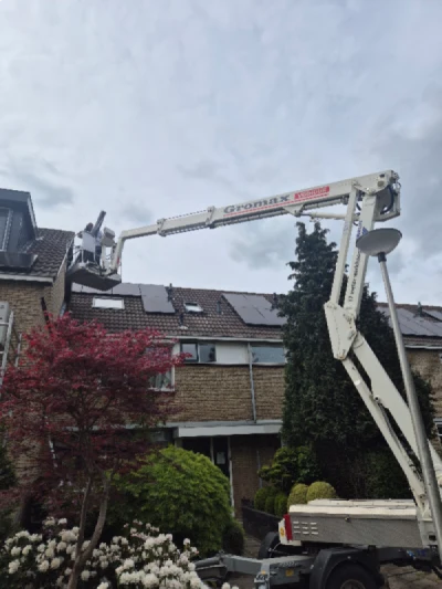 Hoogwerker met monteur voor rijtjeswoning. De monteur plaatst airco koelleiding tegen gevel van 2e verdieping.