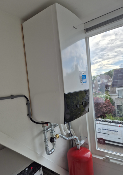 Binnenunit van warmtepomp met daaronder een buffervat en op de achtergrond een busje van Slim Verwarmen