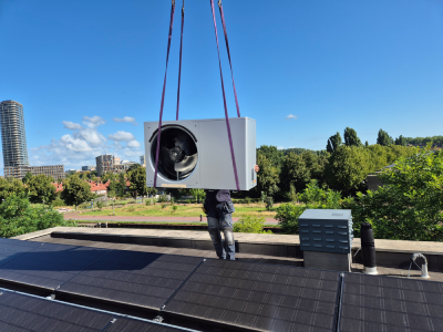 Buitenunit van warmtepomp wordt middels een kraan op een dak geplaatst