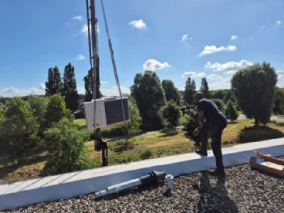 Monteur op dak. Warmtepomp wordt via kraan erheen getransporteerd