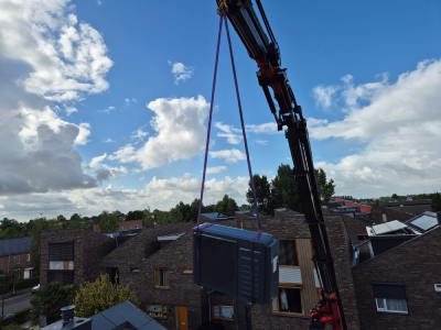 Kraant tilt Intergas Xtend hybride warmtepomp met koelfunctie op een dak. Andere huizen op achtergrond