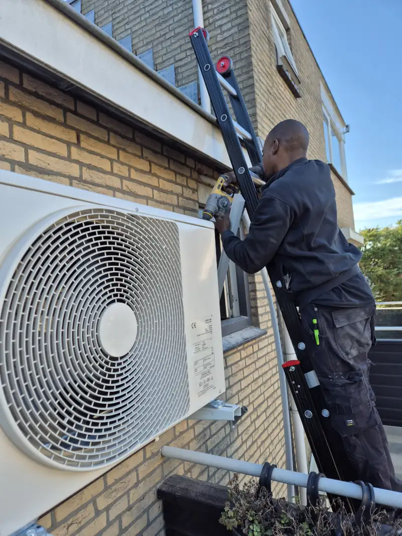 Monteur monteert warmtepomp via ladder tegen gevel